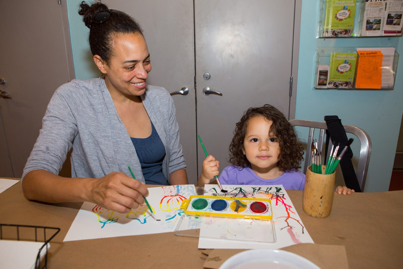 A person and their child are watercolor painting together.