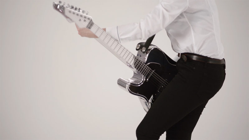 The midsection of a person wearing a white shirt and black pants seen in profile, playing a guitar two necks and strings on both sides