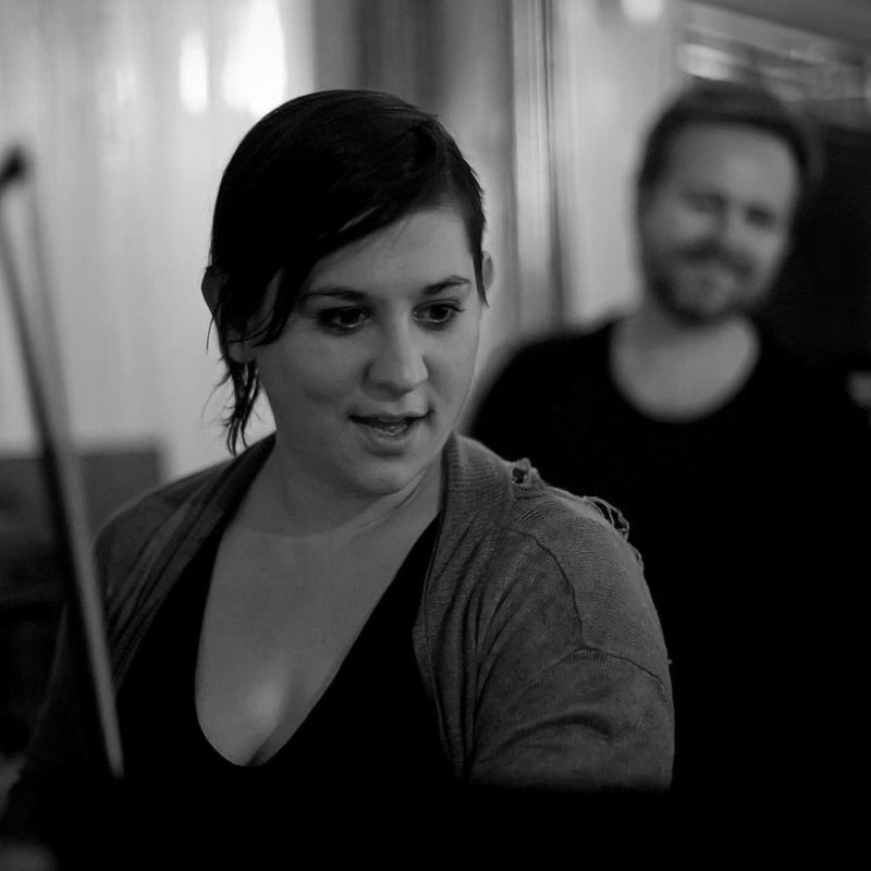 Woman sits in the foreground with a man out of focus behind her.