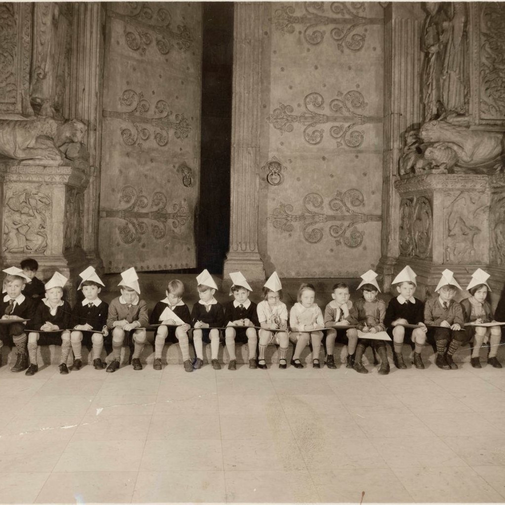 Young art students wearing paper hats sit in a row at the Carnegie Museum of Art Hall of Architecture.
