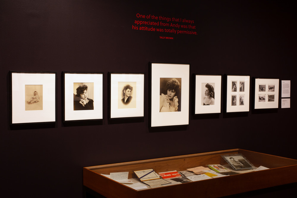 A single row of framed photographs of Tally Brown hang on a dark wall