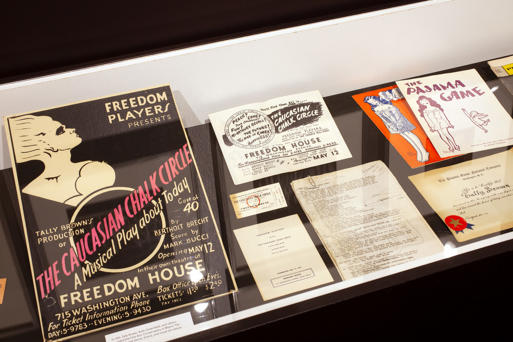 A vitrine containing various theatre-related memorabilia, including programs, a poster, a script, and a flyer.
