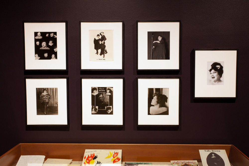 Two rows of photographs of Tally Brown hang on a dark wall