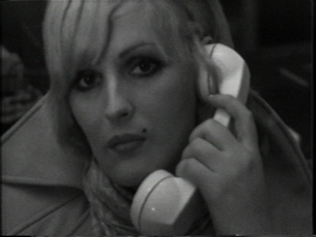 Black and white film still close-up of Candy Darling holding a phone to her ear