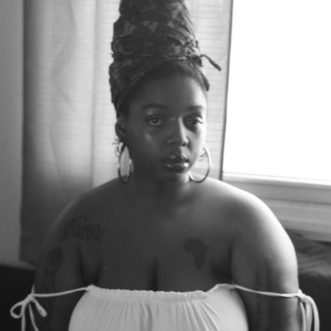 Woman wearing a headwrap sits in front of a window with light coming in.