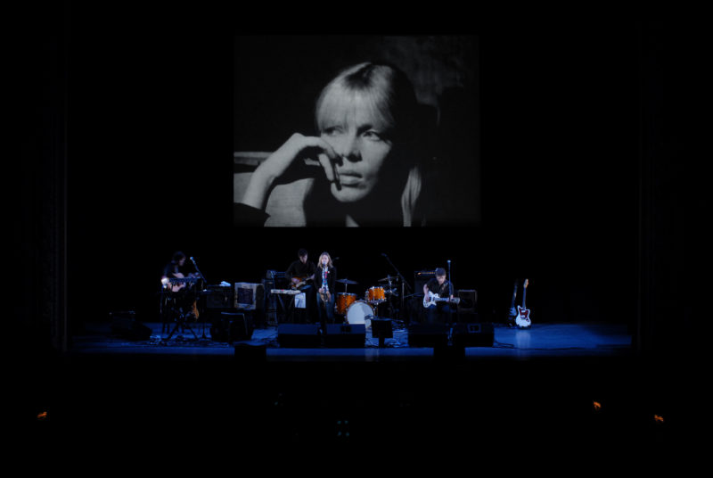 A band performs on a stage in front of a screen that is showing a film.