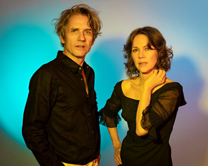 Two people standing in front of a colorful background looking at the camera.