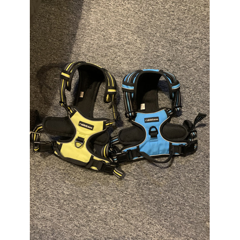 Two dog harnesses sitting side by side, one blue and one yellow
