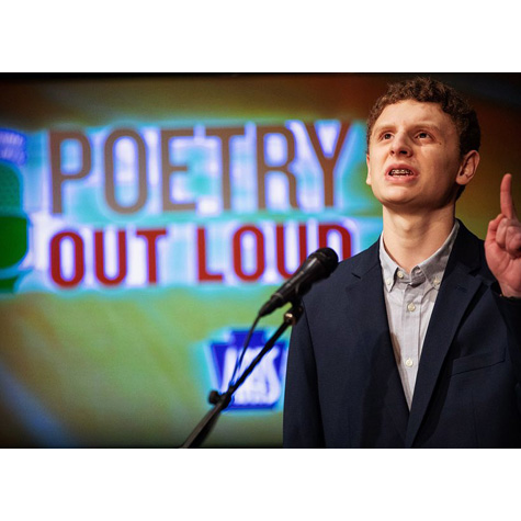 Man in front of a mic with the words poetry out loud behind him