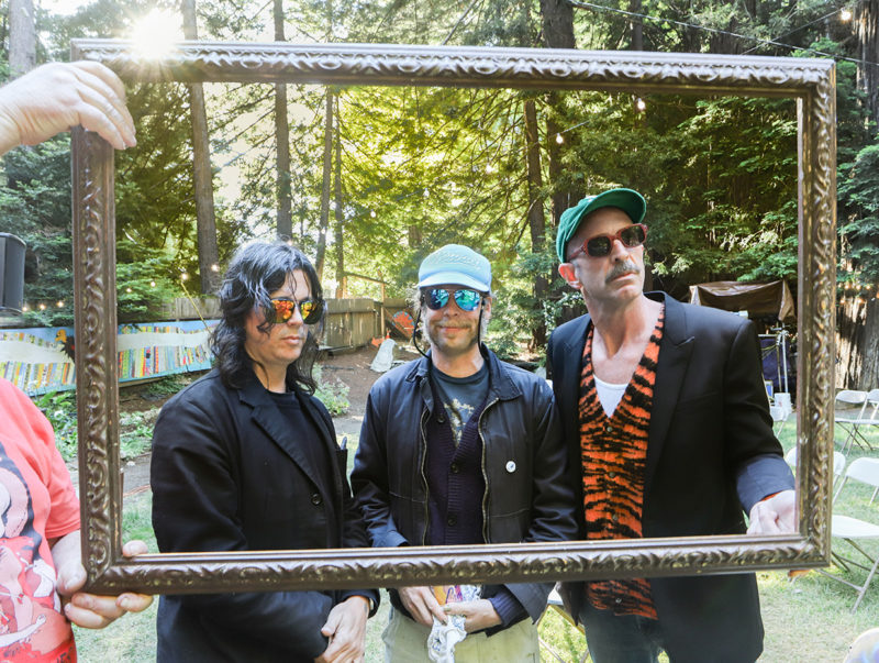 Three people stand outside with a wood picture frame being held in front of them.