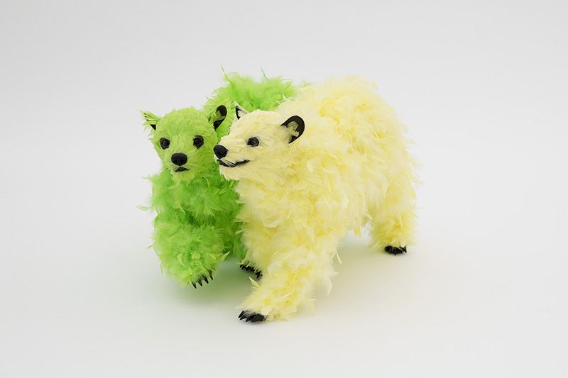 Two foam bear sculptures stand next to each other. One is covered in lime green feathers and the other in yellow feathers.