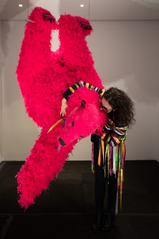 Paola Pivi is standing next to one of her pink bear sculptures. She is holding it around its neck.