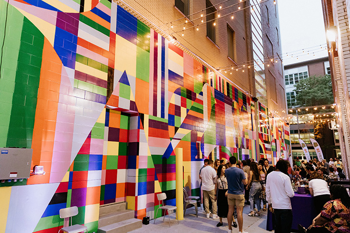 A group of people in an outdoor space with a brightly painted wall mural.