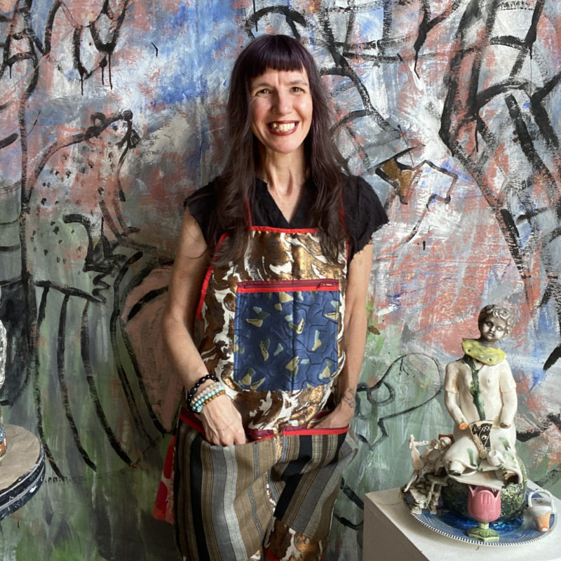 Woman stands against painted canvas in art studio