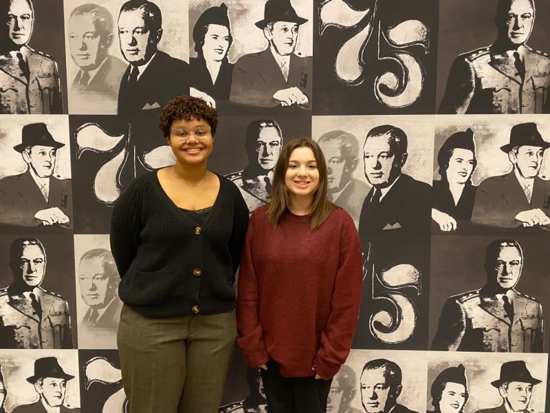 Two young people standing in front of a silkscreen printed mural.