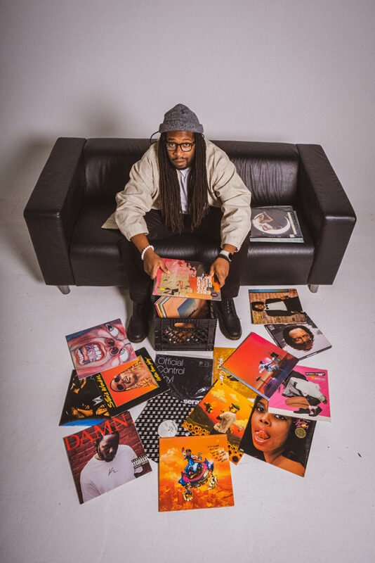Arie Cole sits on a couch with many record albums in front of him.