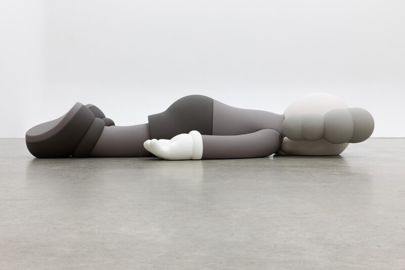 A black and white sculpture of a figure laying flat on their stomach on the floor.