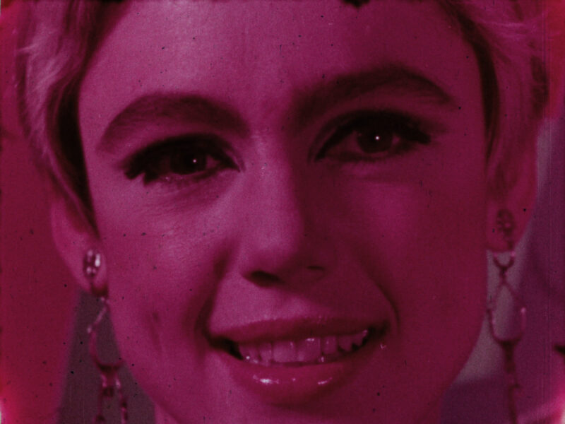 Film still of a close-up of a smiling Edie Sedgwick with a pink tone.