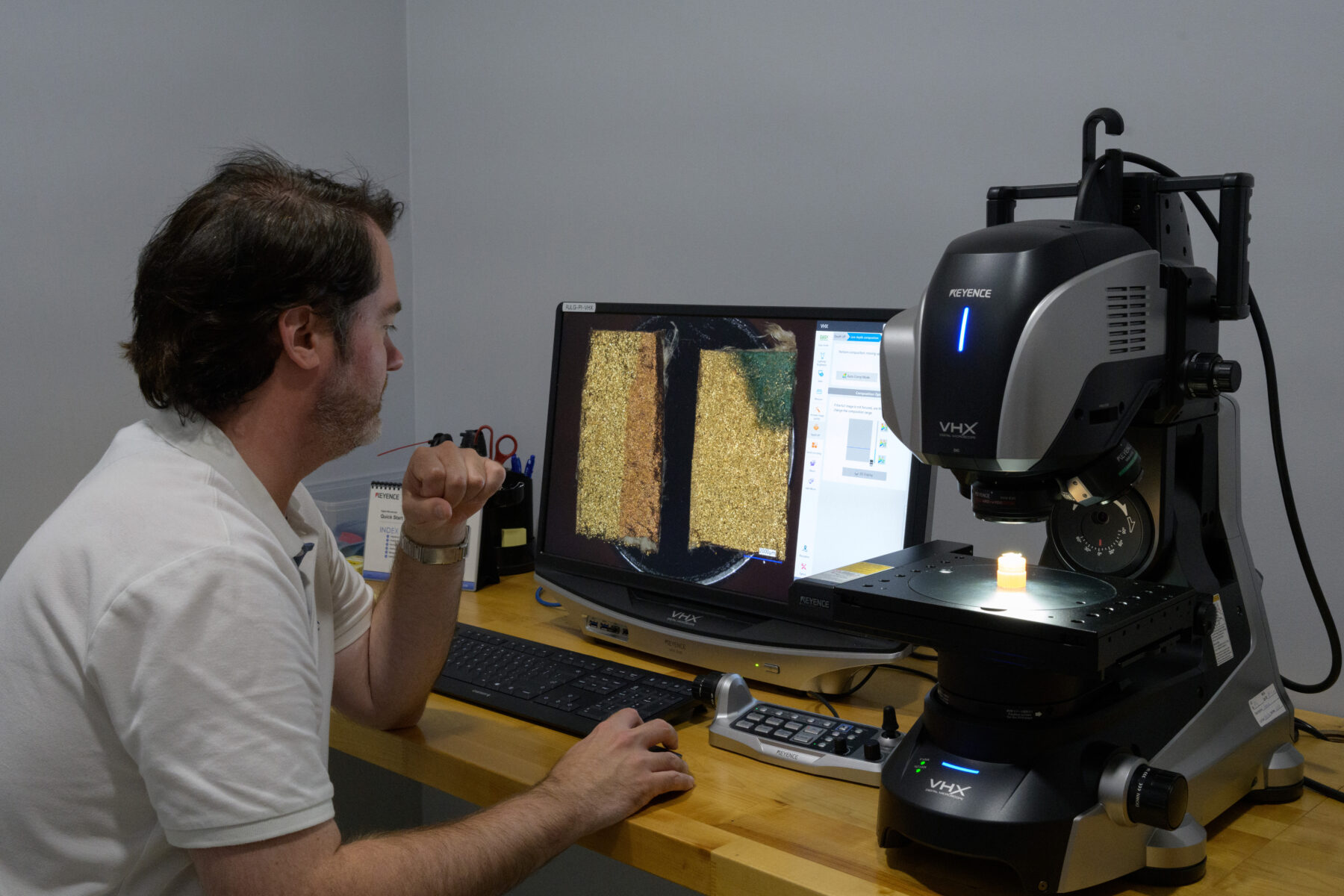 A man sits at a desk using a digital microscope.