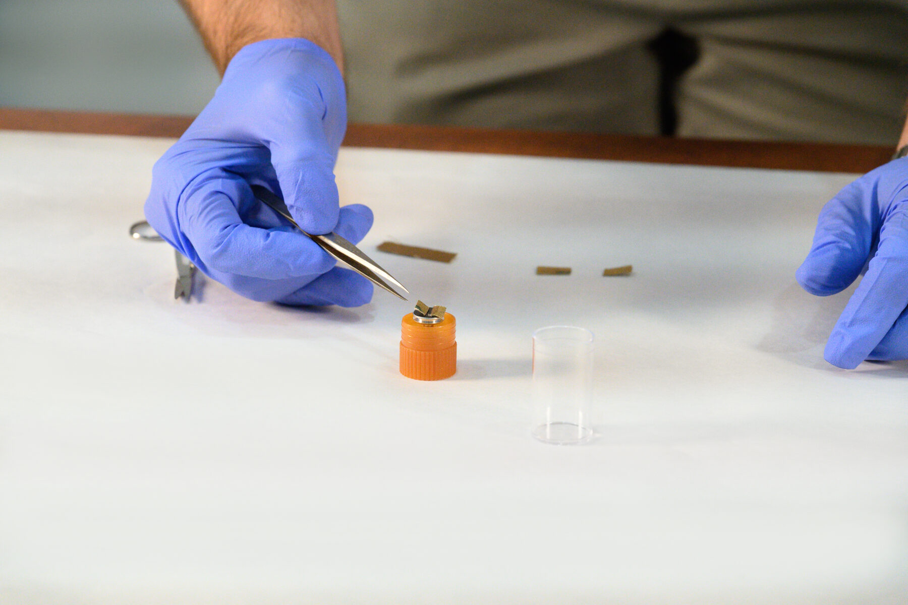 Two purple-gloved hands hold tweezers to place a painting fragment in place.