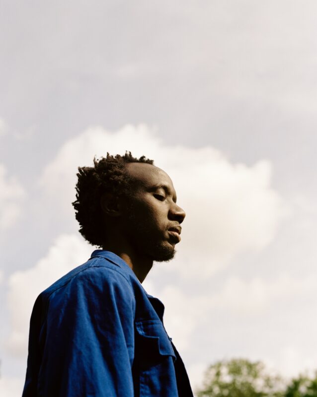 A photo taken from the left side of a person wearing a jean jacket and standing outside. The sky and clouds can be seen in the background.