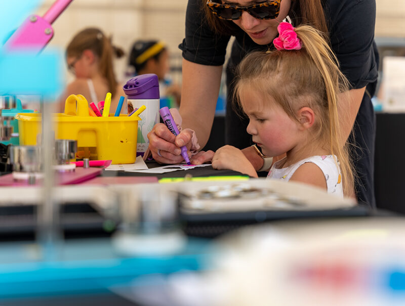 A girl working at a table with art materials, while her mother helps.