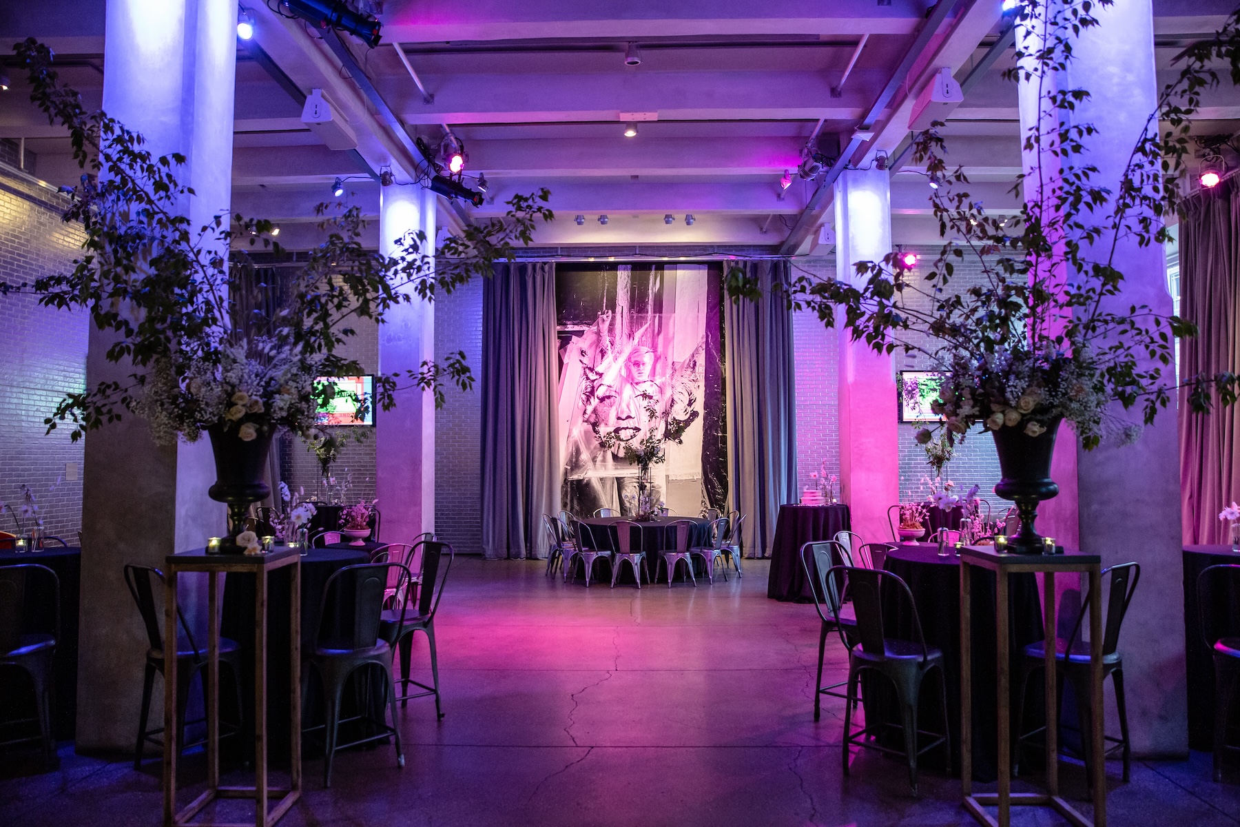 The Andy Warhol Museum's entrance space decorated with tables and floral arrangements accented with magenta overhead lights.