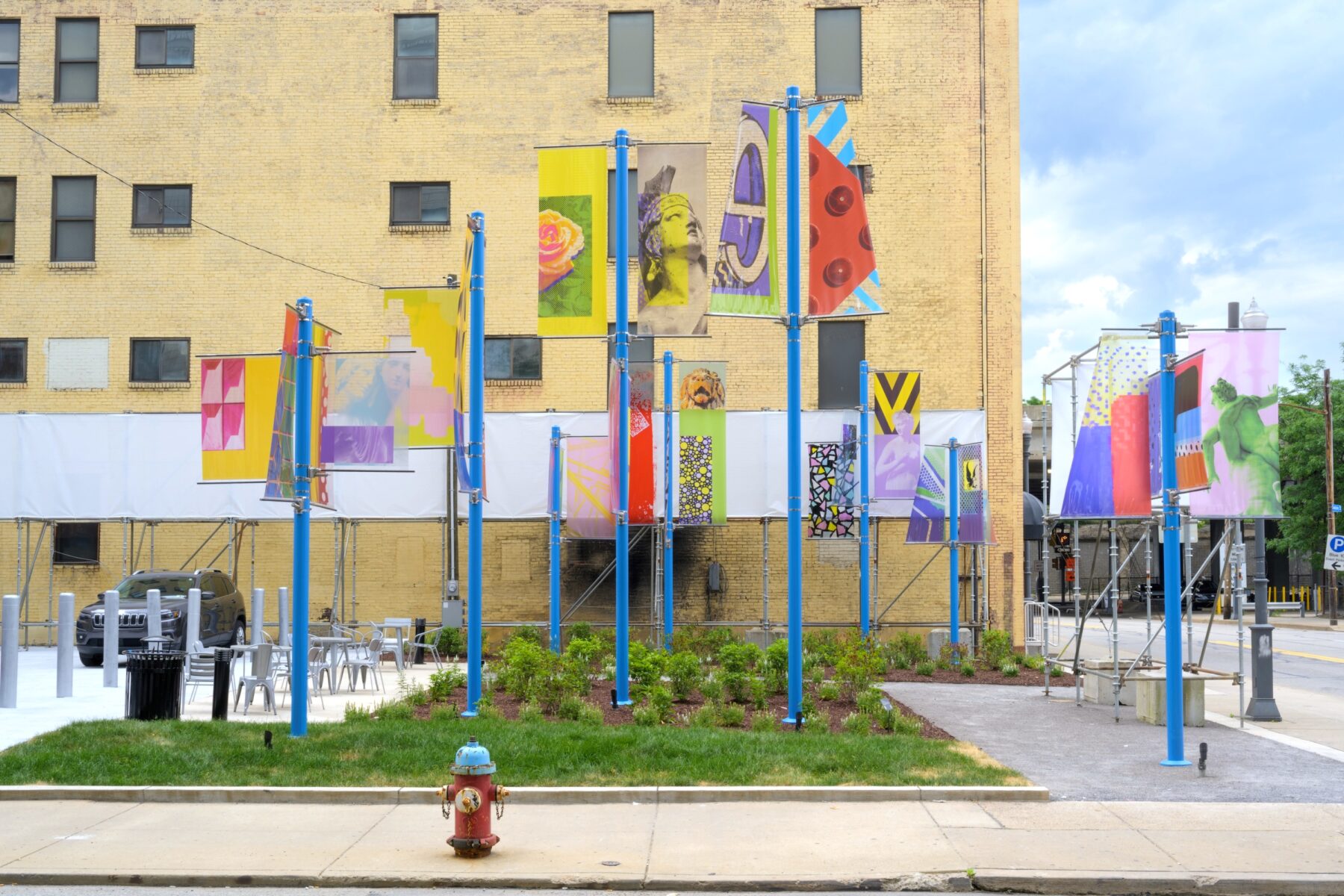 Installation image of art on 9 blue poles each with two colorful transparent banners that have various images on them.