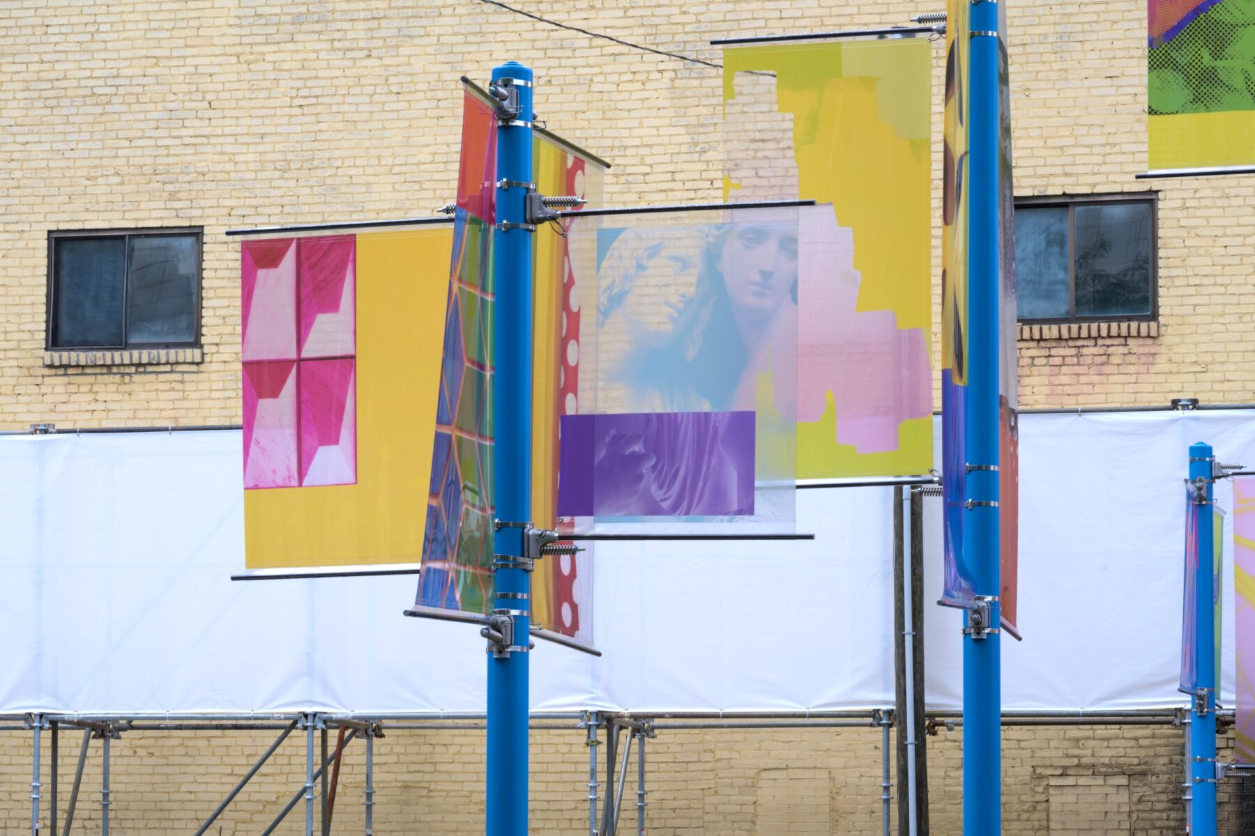 Installation image of art on 2 blue poles each with two colorful transparent banners that have various images on them.