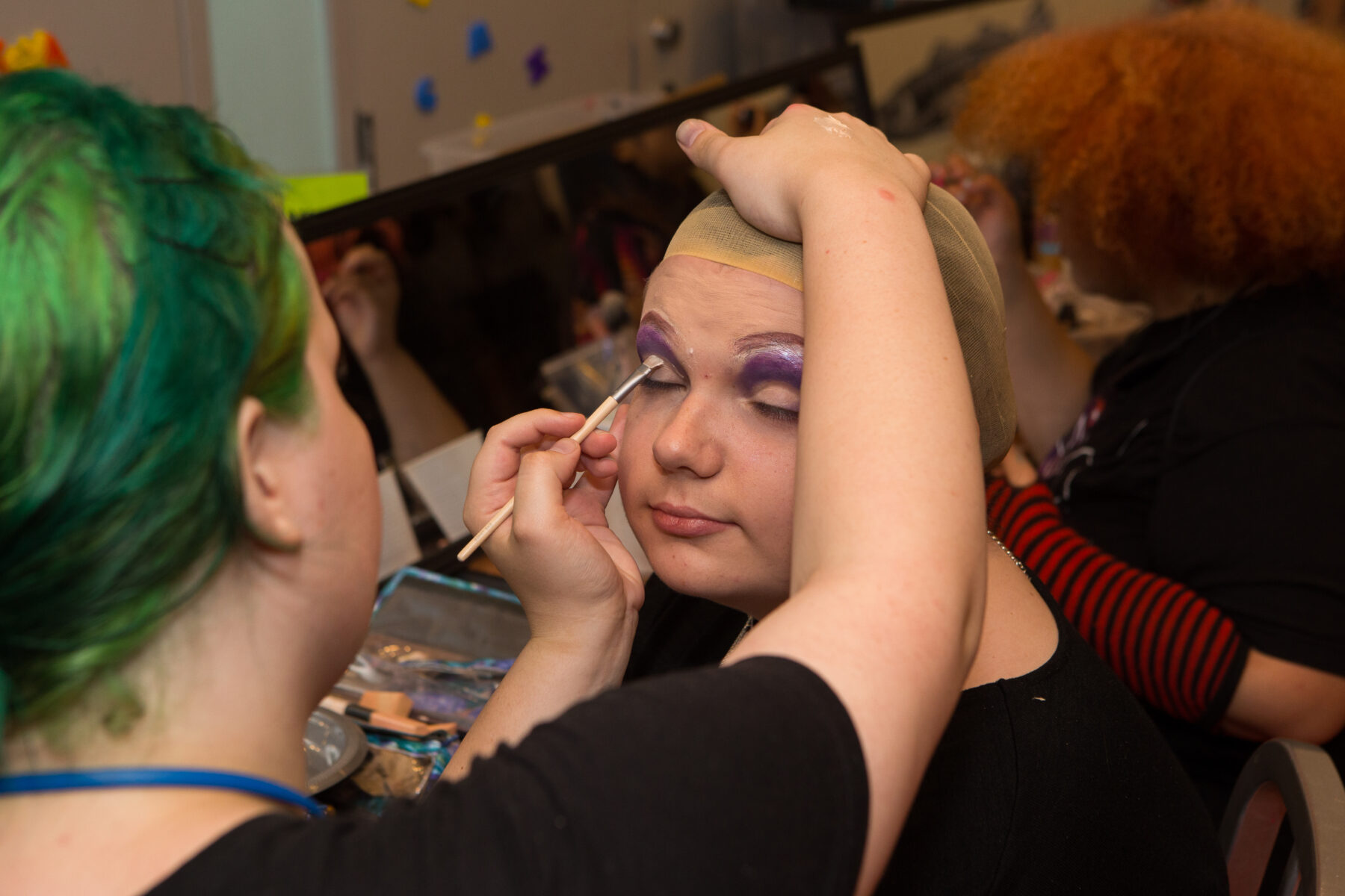 Person (on left) applying eye shadow to a person in the center of the image