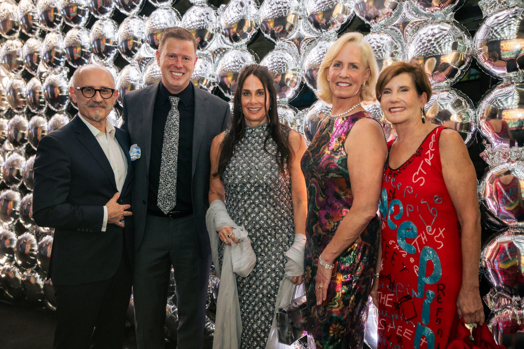 Five people pose infront of a wall of silver balloons