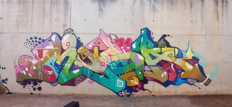 Colorful graffiti artwork on a concrete wall featuring intricate lettering and abstract design elements.