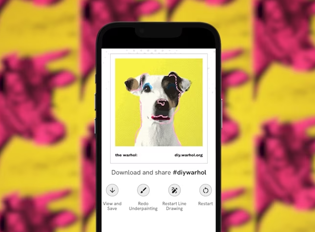 A phone showing an image of a dog that is styled like an Andy Warhol portrait. In the background is a bright yellow and pink pattern of Cows by Andy Warhol.
