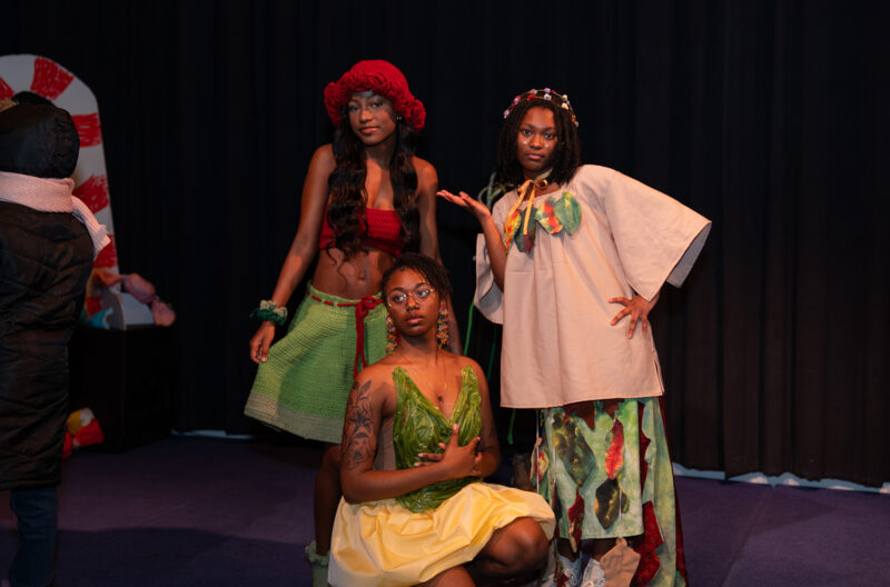 hree individuals in colorful, artistic costumes pose on a stage.