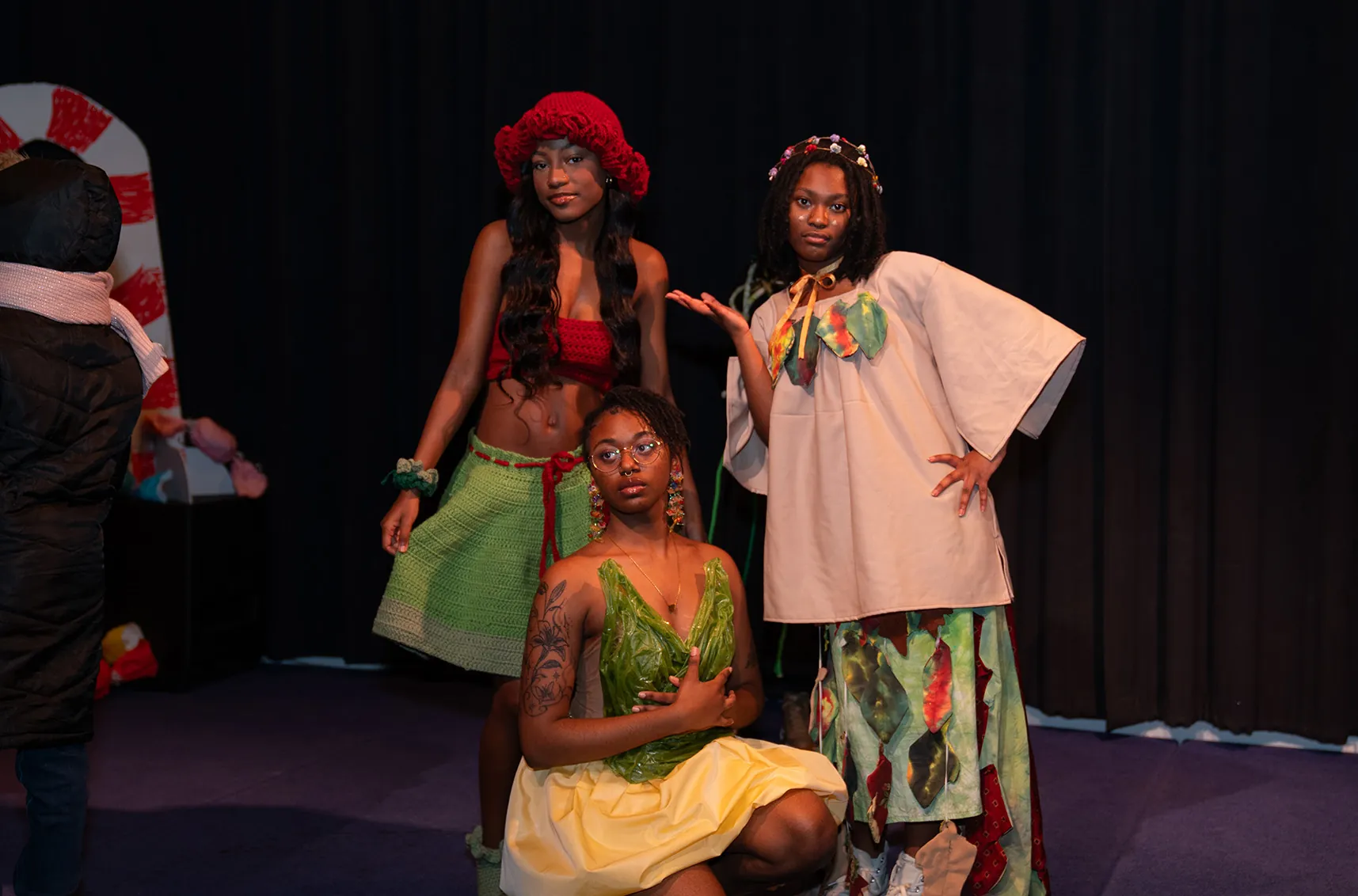 Three individuals in colorful, artistic costumes pose on a stage.