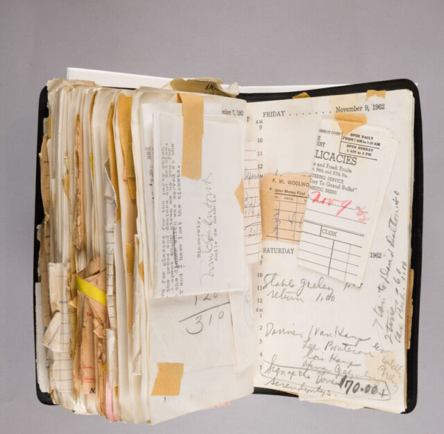 A note book opened to a later page. It is full of notes, papers and receipts taped onto the page.