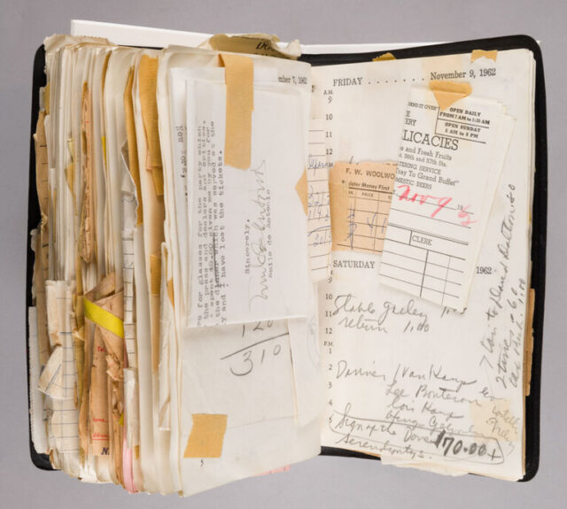 A note book opened to a later page. It is full of notes, papers and receipts taped onto the page.