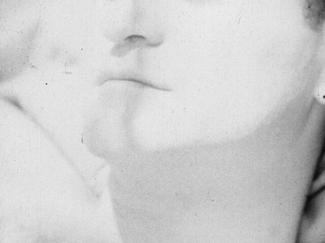 A black and white film still of a man's chin. The image is so bright it almost obscures the details.