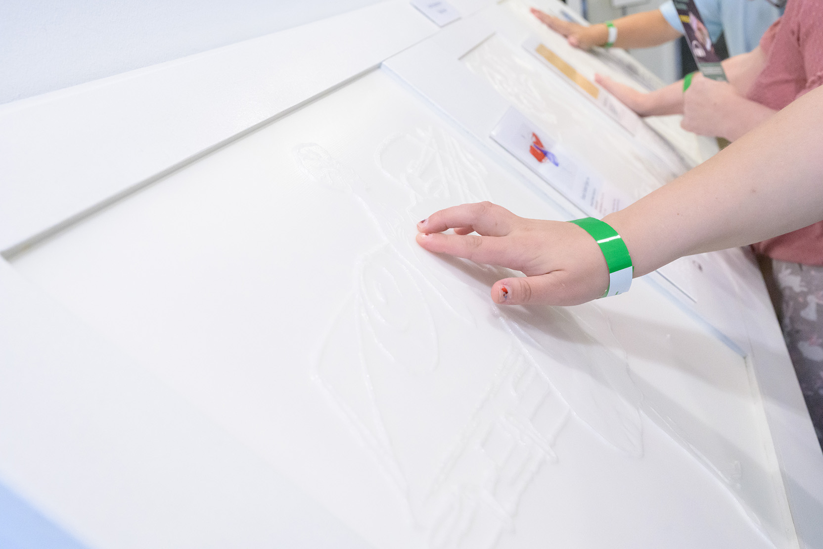 A person with a green wristband touches a textured, tactile illustration designed for accessibility in a a gallery at The Warhol.