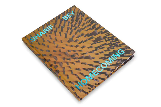 An orange and brown cover of a hardback book with the text Sharif Bey Homecoming. The cover image appears to be spikes pushed into yellow/orange clay.